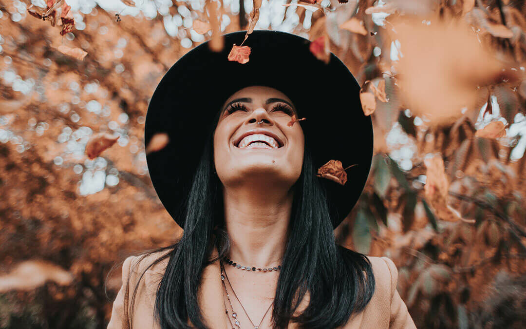 Woman smiling with autumn leaves falling around her